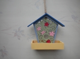 Blue, green and yellow wooden bird feeder with pink flowers